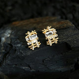 These 18k real gold-plated stud earrings feature an intricate geometric woven design, crafted with twisted gold tones that create a luxurious, textured look. Adorned with a central rectangular baguette-cut zirconia stone surrounded by round pavé-set zircons, they sparkle brilliantly with a blend of clear cubic zirconia and golden metalwork. The elegant yet bold silhouette combines modern geometry with timeless glamour, making it a striking accessory.