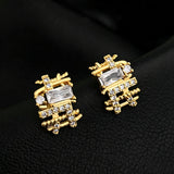 These 18k real gold-plated stud earrings feature an intricate geometric woven design, crafted with twisted gold tones that create a luxurious, textured look. Adorned with a central rectangular baguette-cut zirconia stone surrounded by round pavé-set zircons, they sparkle brilliantly with a blend of clear cubic zirconia and golden metalwork. The elegant yet bold silhouette combines modern geometry with timeless glamour, making it a striking accessory.
