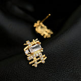 These 18k real gold-plated stud earrings feature an intricate geometric woven design, crafted with twisted gold tones that create a luxurious, textured look. Adorned with a central rectangular baguette-cut zirconia stone surrounded by round pavé-set zircons, they sparkle brilliantly with a blend of clear cubic zirconia and golden metalwork. The elegant yet bold silhouette combines modern geometry with timeless glamour, making it a striking accessory.