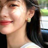 These 18k real gold-plated stud earrings feature an intricate geometric woven design, crafted with twisted gold tones that create a luxurious, textured look. Adorned with a central rectangular baguette-cut zirconia stone surrounded by round pavé-set zircons, they sparkle brilliantly with a blend of clear cubic zirconia and golden metalwork. The elegant yet bold silhouette combines modern geometry with timeless glamour, making it a striking accessory.