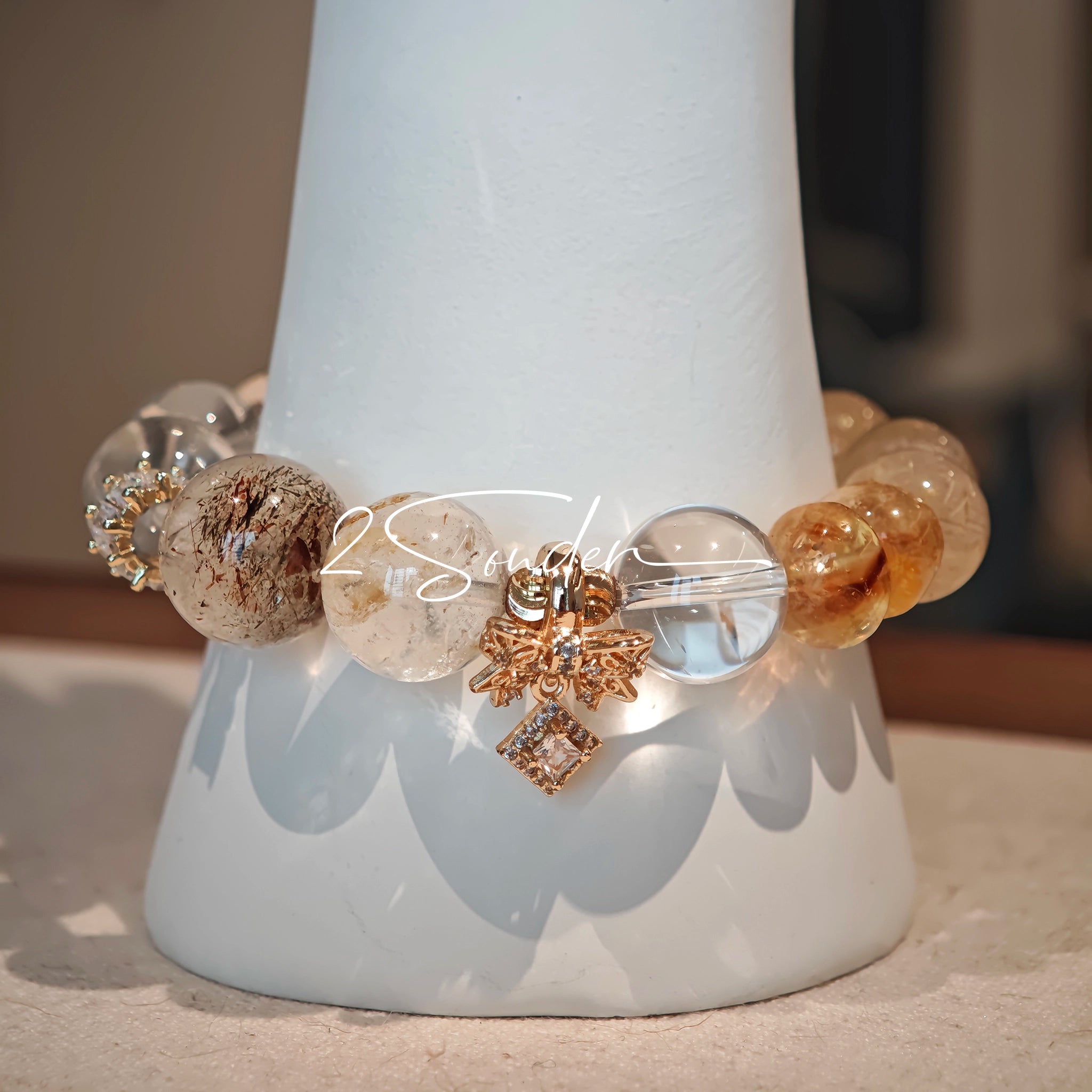 This is a gemstone bracelet made of Golden Hematoid Quartz, Copper Rutilated Quartz, Clear Quartz and Citrine. In the bracelet, there is also a bow pendant as decoration.