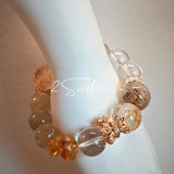 This is a gemstone bracelet made of Golden Hematoid Quartz, Copper Rutilated Quartz, Clear Quartz and Citrine. In the bracelet, there is also a bow pendant as decoration.