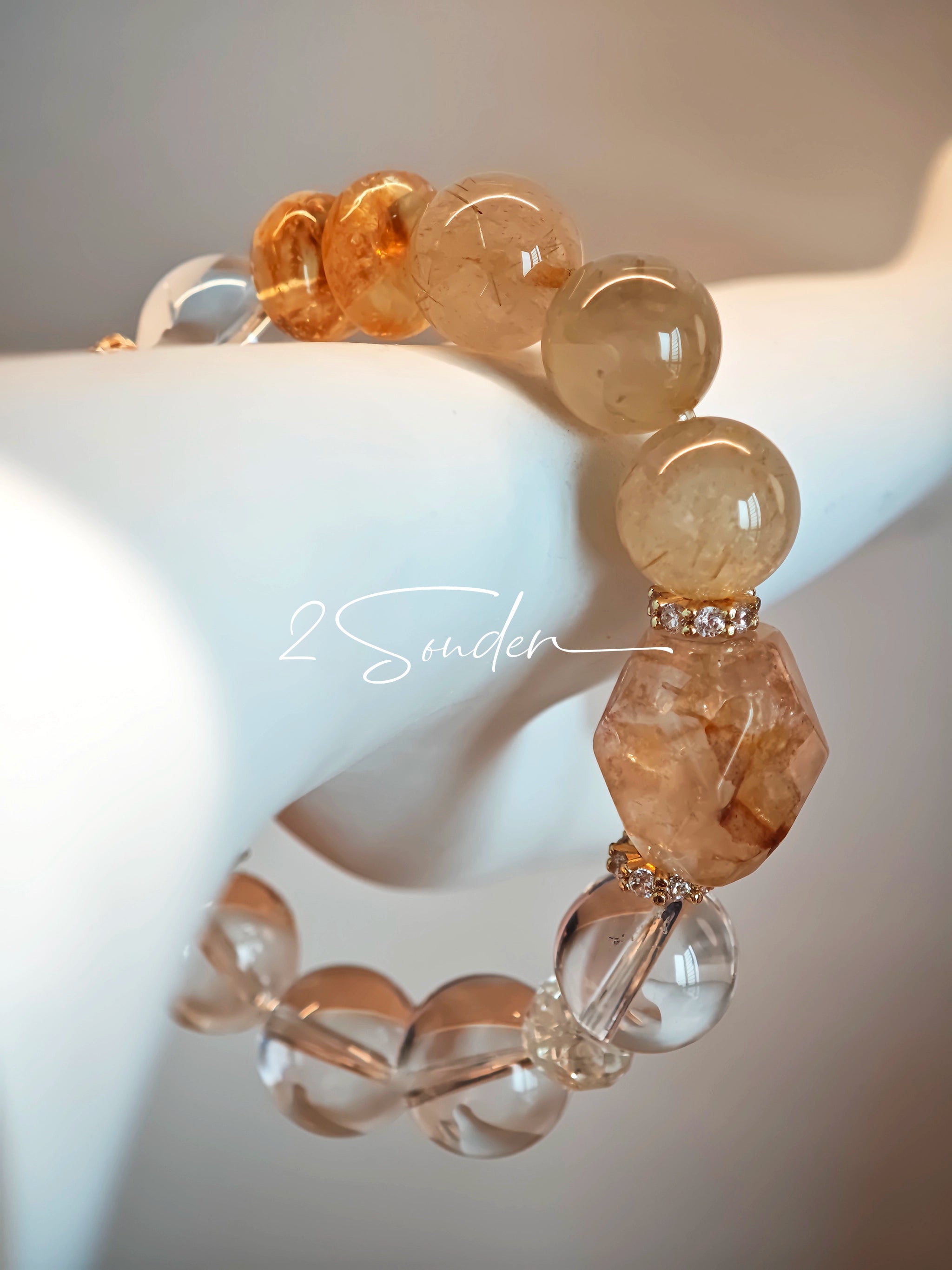 This is a gemstone bracelet made of Golden Hematoid Quartz, Copper Rutilated Quartz, Clear Quartz and Citrine. In the bracelet, there is also a bow pendant as decoration.