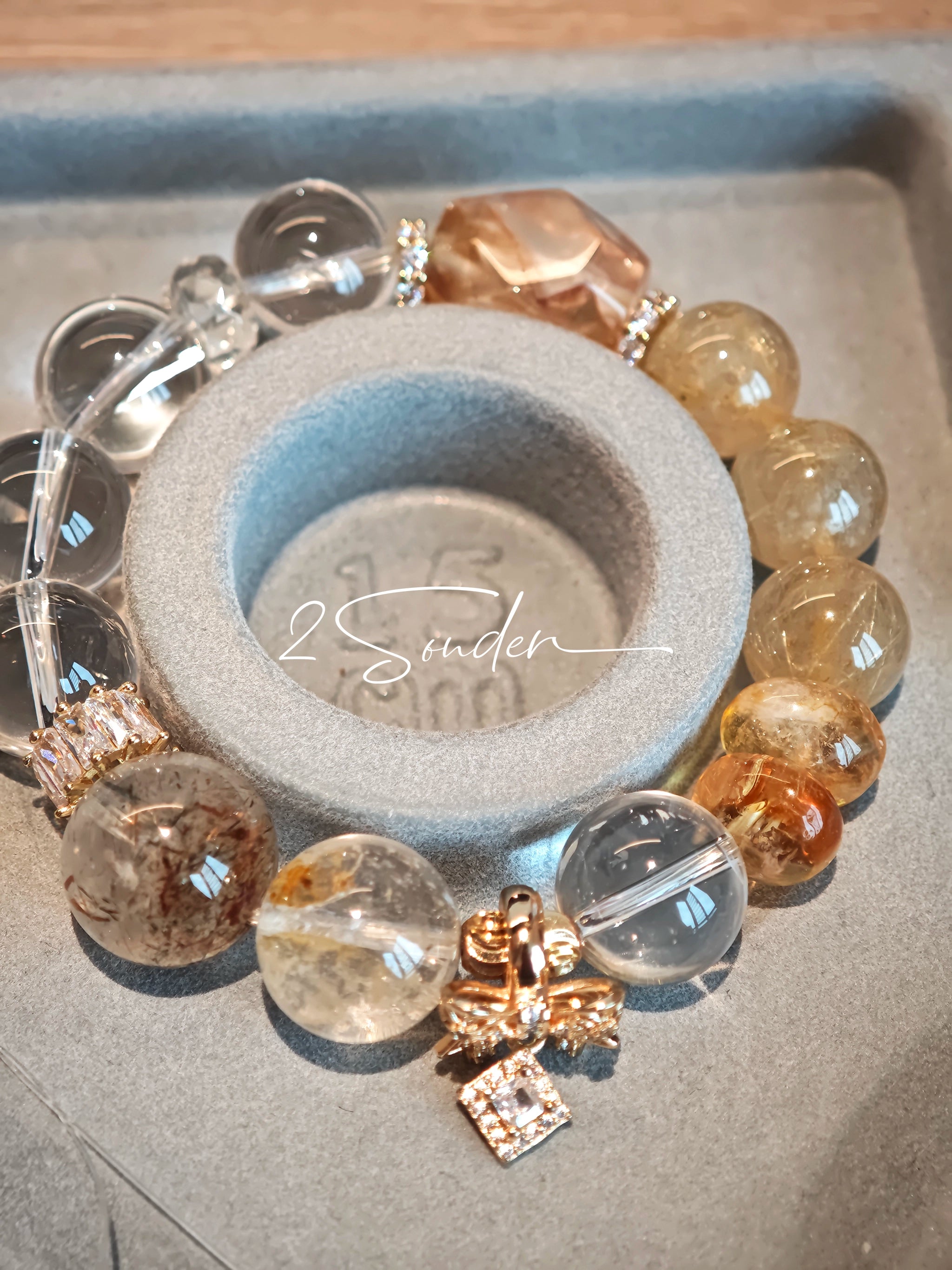 This is a gemstone bracelet made of Golden Hematoid Quartz, Copper Rutilated Quartz, Clear Quartz and Citrine. In the bracelet, there is also a bow pendant as decoration.