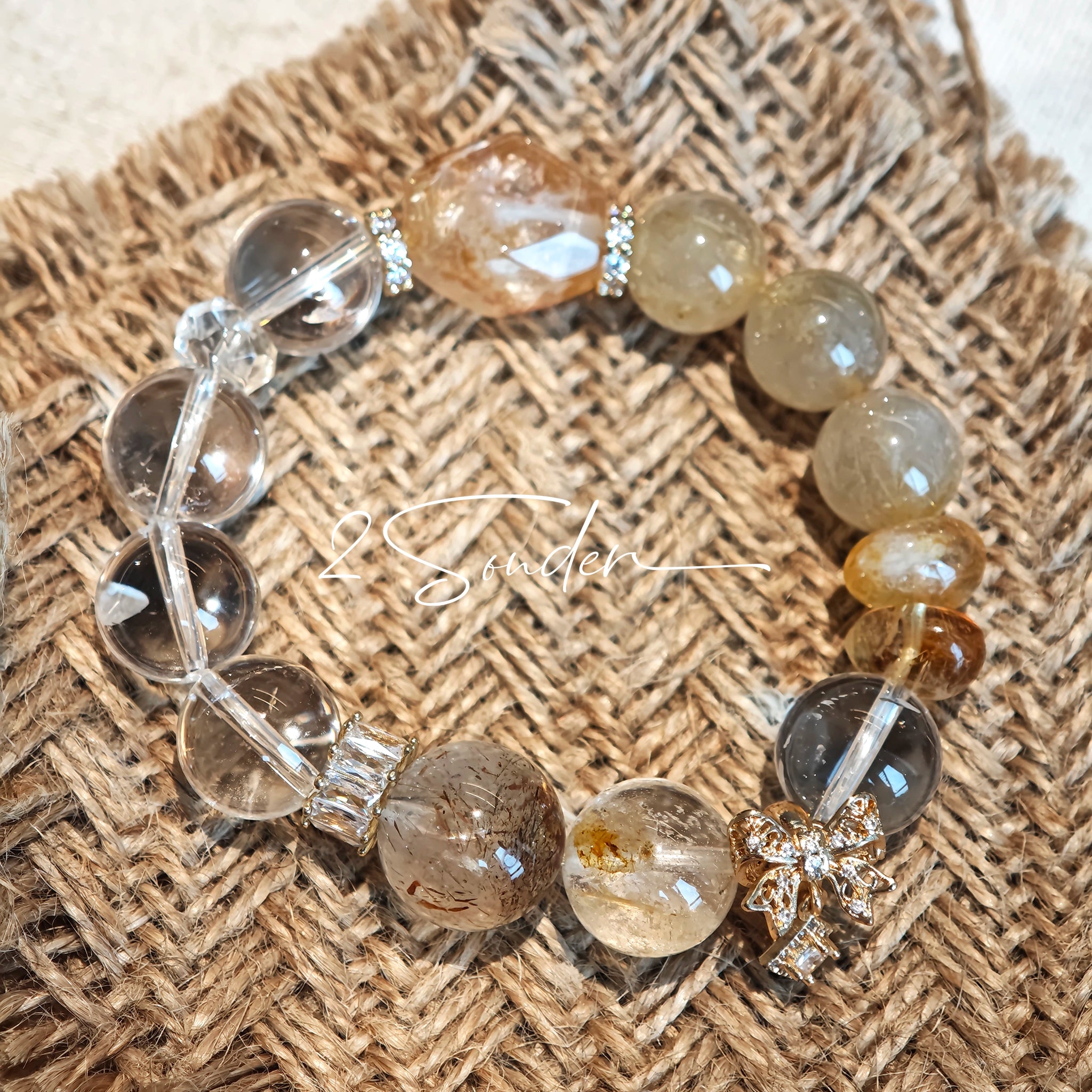 This is a gemstone bracelet made of Golden Hematoid Quartz, Copper Rutilated Quartz, Clear Quartz and Citrine. In the bracelet, there is also a bow pendant as decoration.