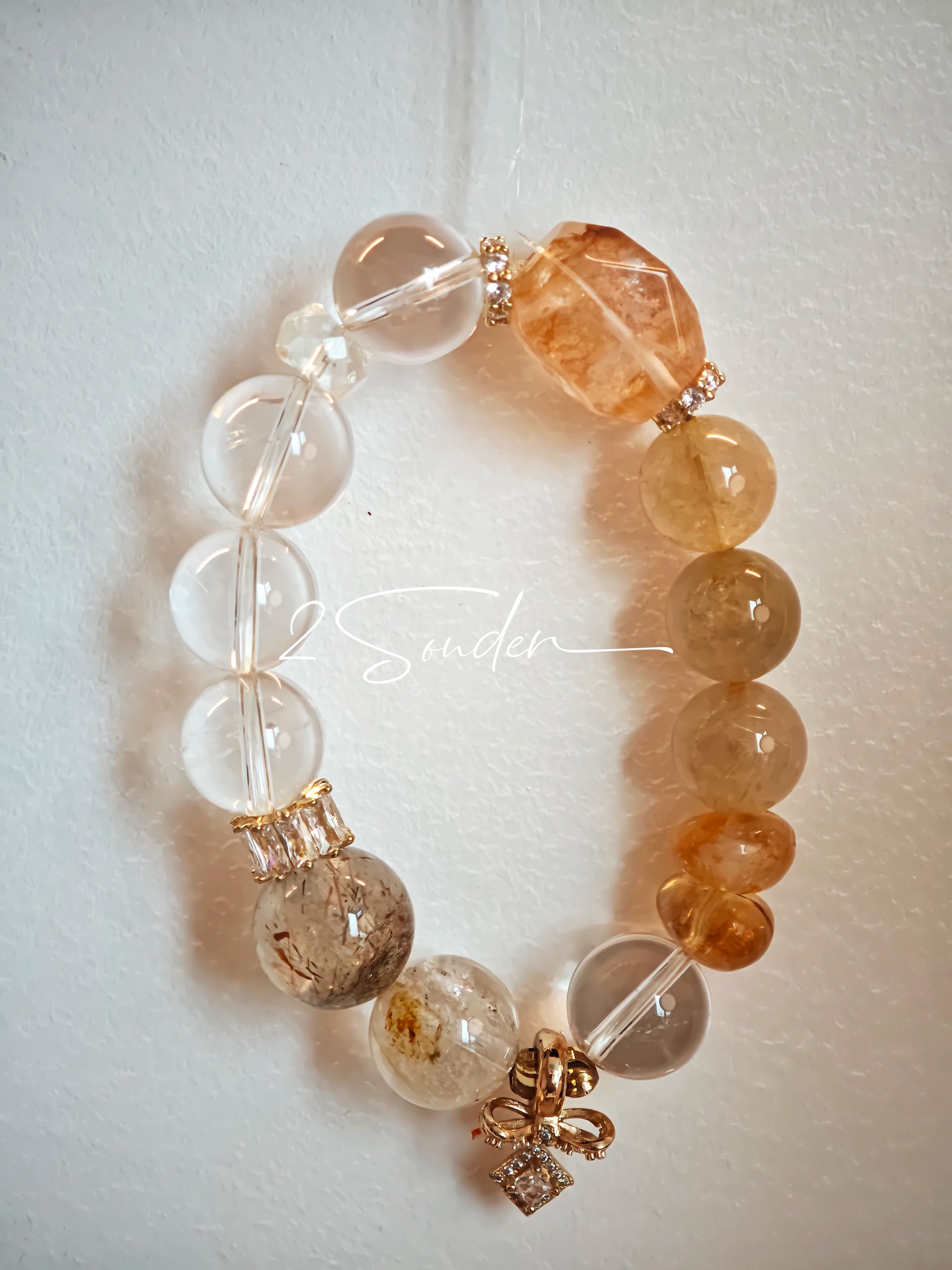 This is a gemstone bracelet made of Golden Hematoid Quartz, Copper Rutilated Quartz, Clear Quartz and Citrine. In the bracelet, there is also a bow pendant as decoration.