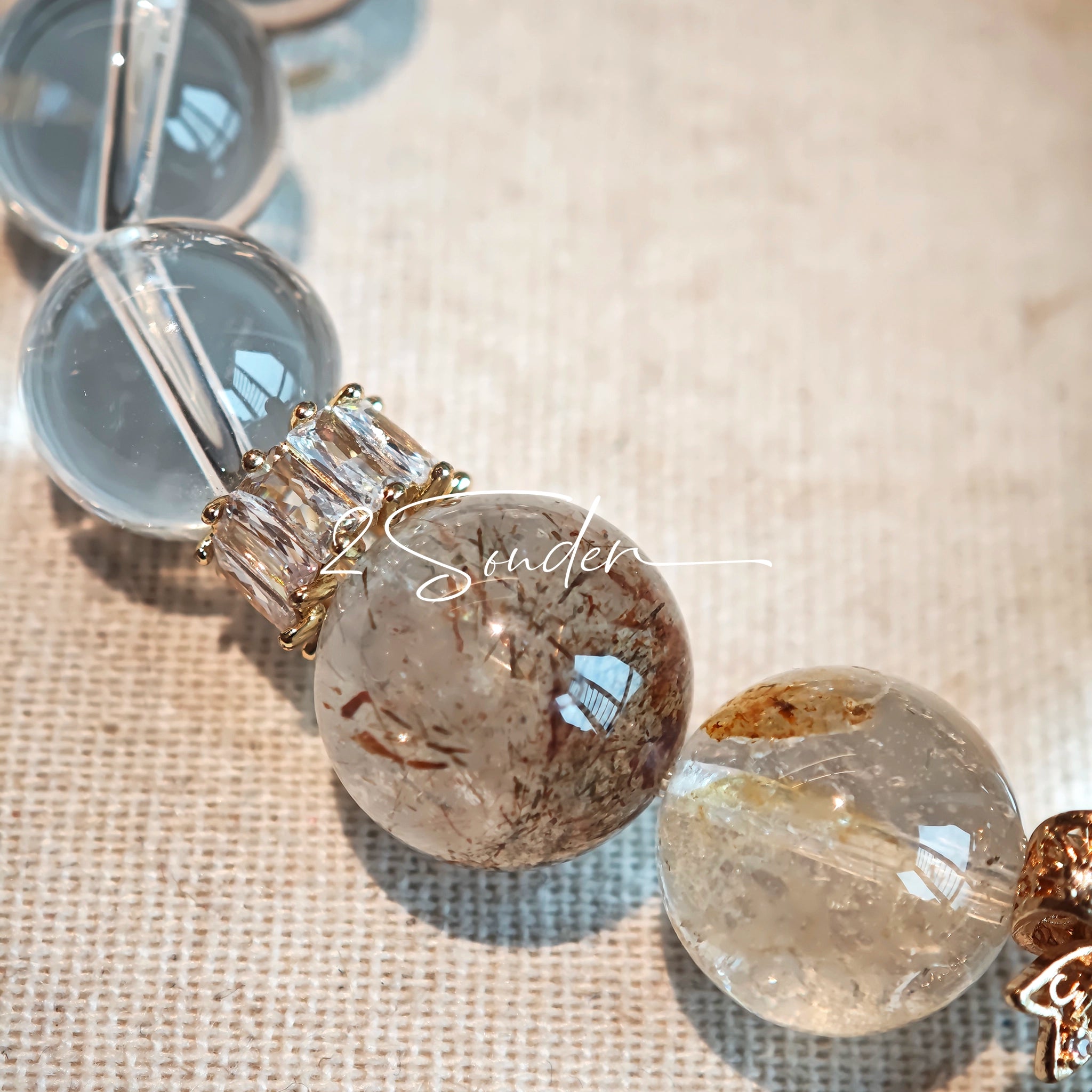 This is a gemstone bracelet made of Golden Hematoid Quartz, Copper Rutilated Quartz, Clear Quartz and Citrine. In the bracelet, there is also a bow pendant as decoration.