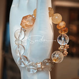 This is a gemstone bracelet made of Golden Hematoid Quartz, Copper Rutilated Quartz, Clear Quartz and Citrine. In the bracelet, there is also a bow pendant as decoration.