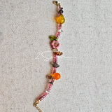This is a bracelet consist of glass beads. The main color of the bracelet is pink. It's also decorated with orange, yellow pear, grey flower, brown leaves and green leaves spacers.