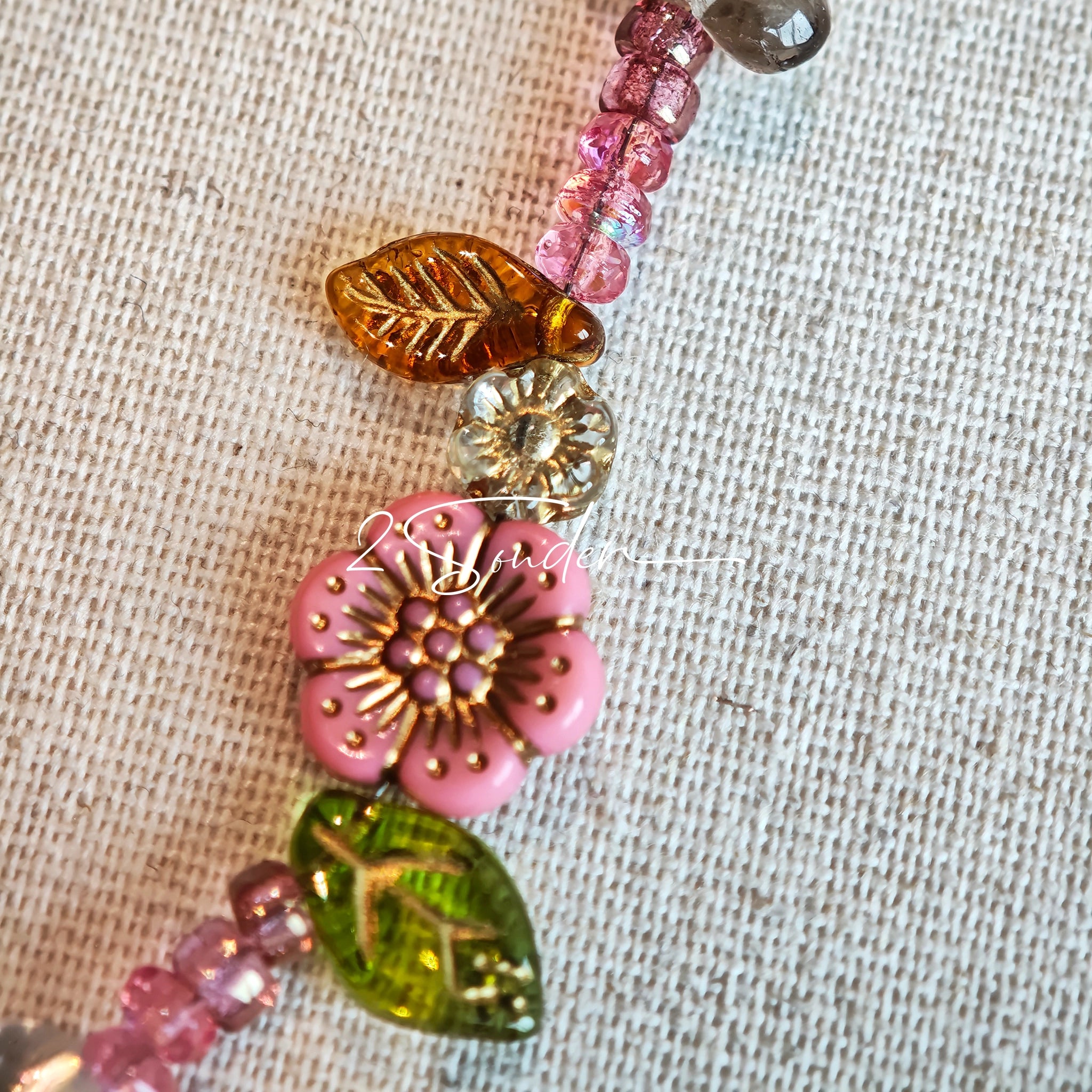 This is a bracelet consist of glass beads. The main color of the bracelet is pink. It's also decorated with orange, yellow pear, grey flower, brown leaves and green leaves spacers.