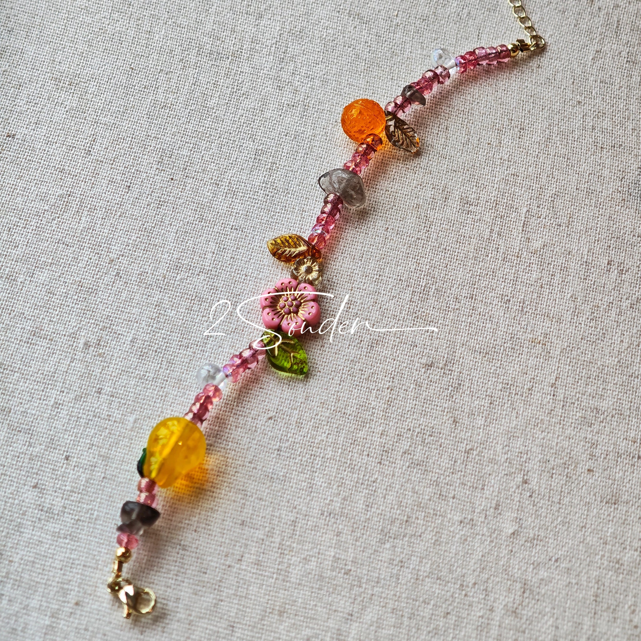 This is a bracelet consist of glass beads. The main color of the bracelet is pink. It's also decorated with orange, yellow pear, grey flower, brown leaves and green leaves spacers.