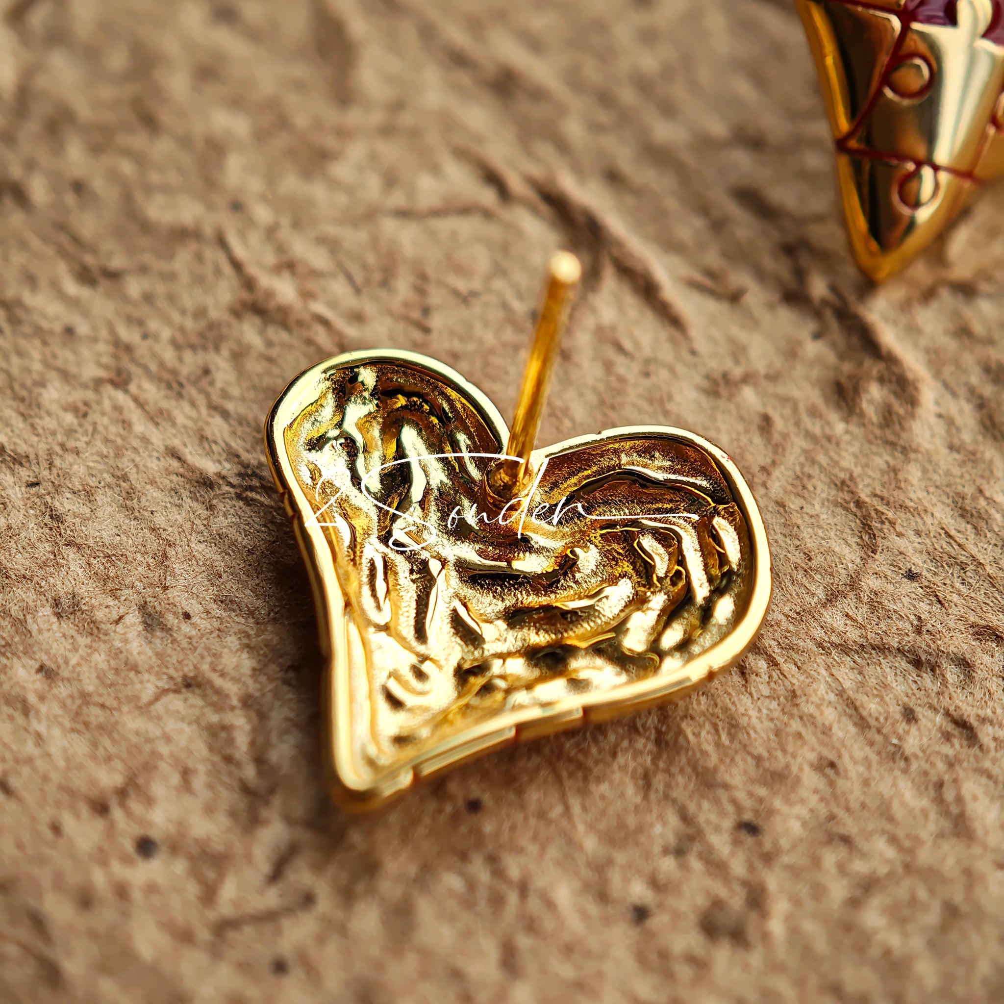 This is a pair of heart earrings with puzzle blocks pattern on the surface. The earrings feature a vibrant enamel center that mimics a beating heart flowing with love. The material of the earrings is sterling silver and enamel, and the color is vintage gold color