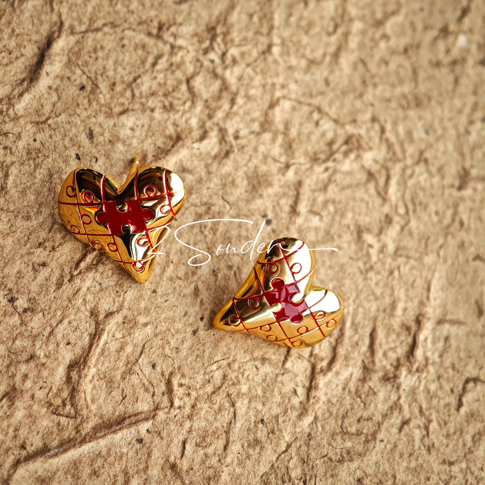 This is a pair of heart earrings with puzzle blocks pattern on the surface. The earrings feature a vibrant enamel center that mimics a beating heart flowing with love. The material of the earrings is sterling silver and enamel, and the color is vintage gold color