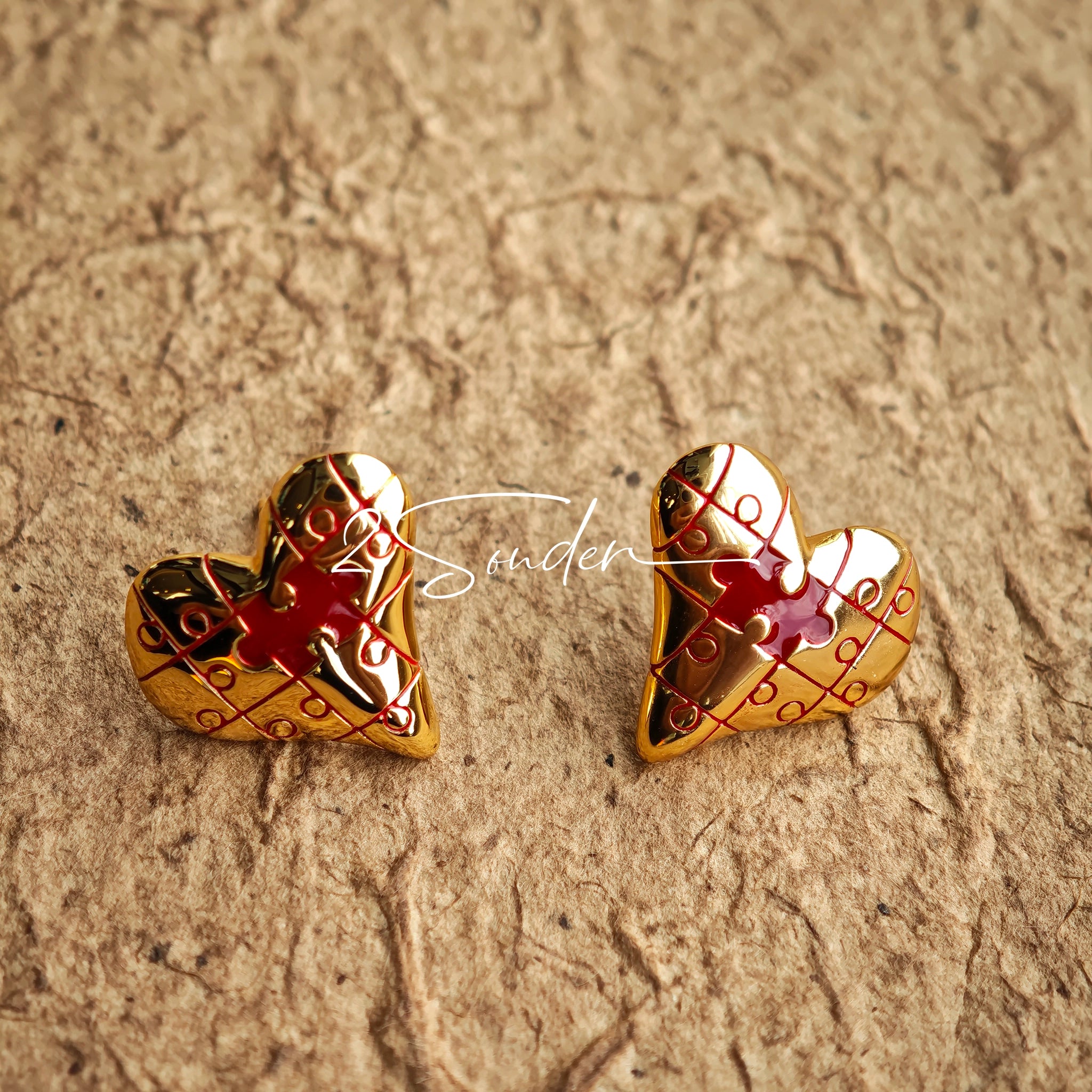 This is a pair of heart earrings with puzzle blocks pattern on the surface. The earrings feature a vibrant enamel center that mimics a beating heart flowing with love. The material of the earrings is sterling silver and enamel, and the color is vintage gold color