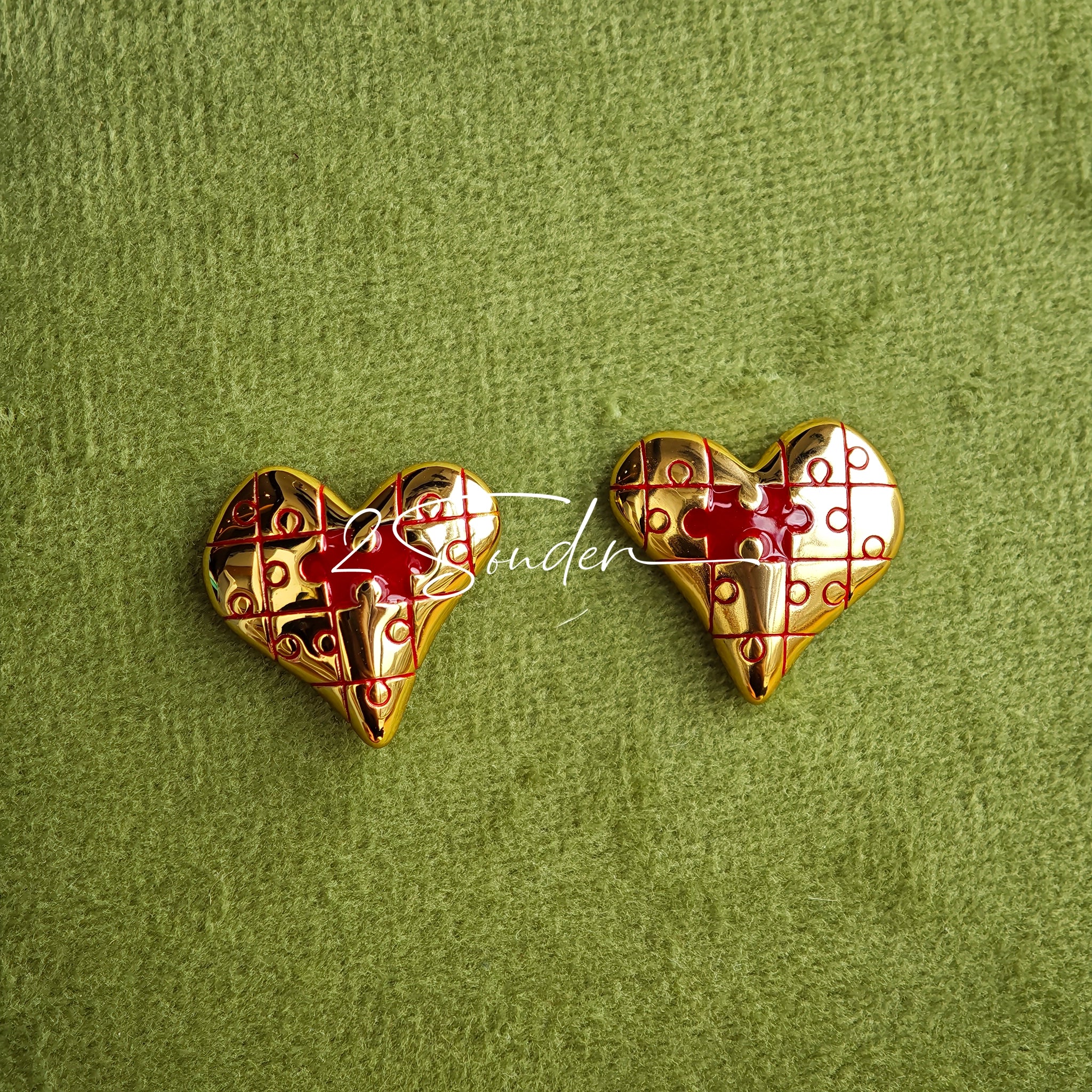 This is a pair of heart earrings with puzzle blocks pattern on the surface. The earrings feature a vibrant enamel center that mimics a beating heart flowing with love. The material of the earrings is sterling silver and enamel, and the color is vintage gold color