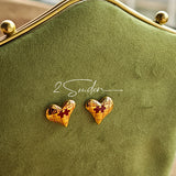 This is a pair of heart earrings with puzzle blocks pattern on the surface. The earrings feature a vibrant enamel center that mimics a beating heart flowing with love. The material of the earrings is sterling silver and enamel, and the color is vintage gold color