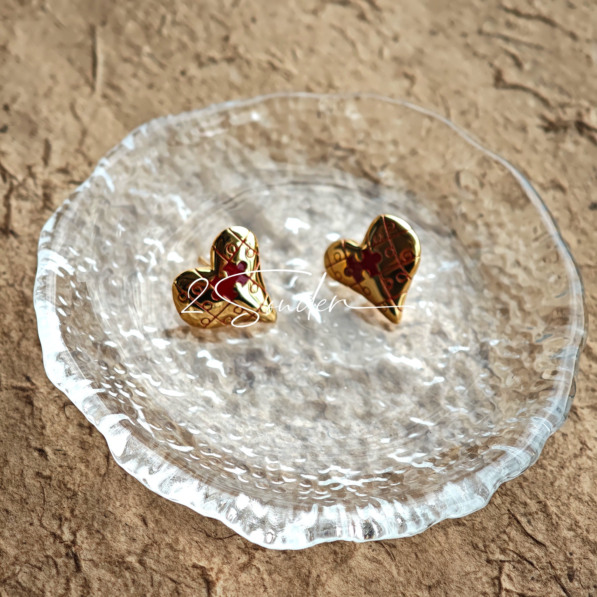 This is a pair of heart earrings with puzzle blocks pattern on the surface. The earrings feature a vibrant enamel center that mimics a beating heart flowing with love. The material of the earrings is sterling silver and enamel, and the color is vintage gold color