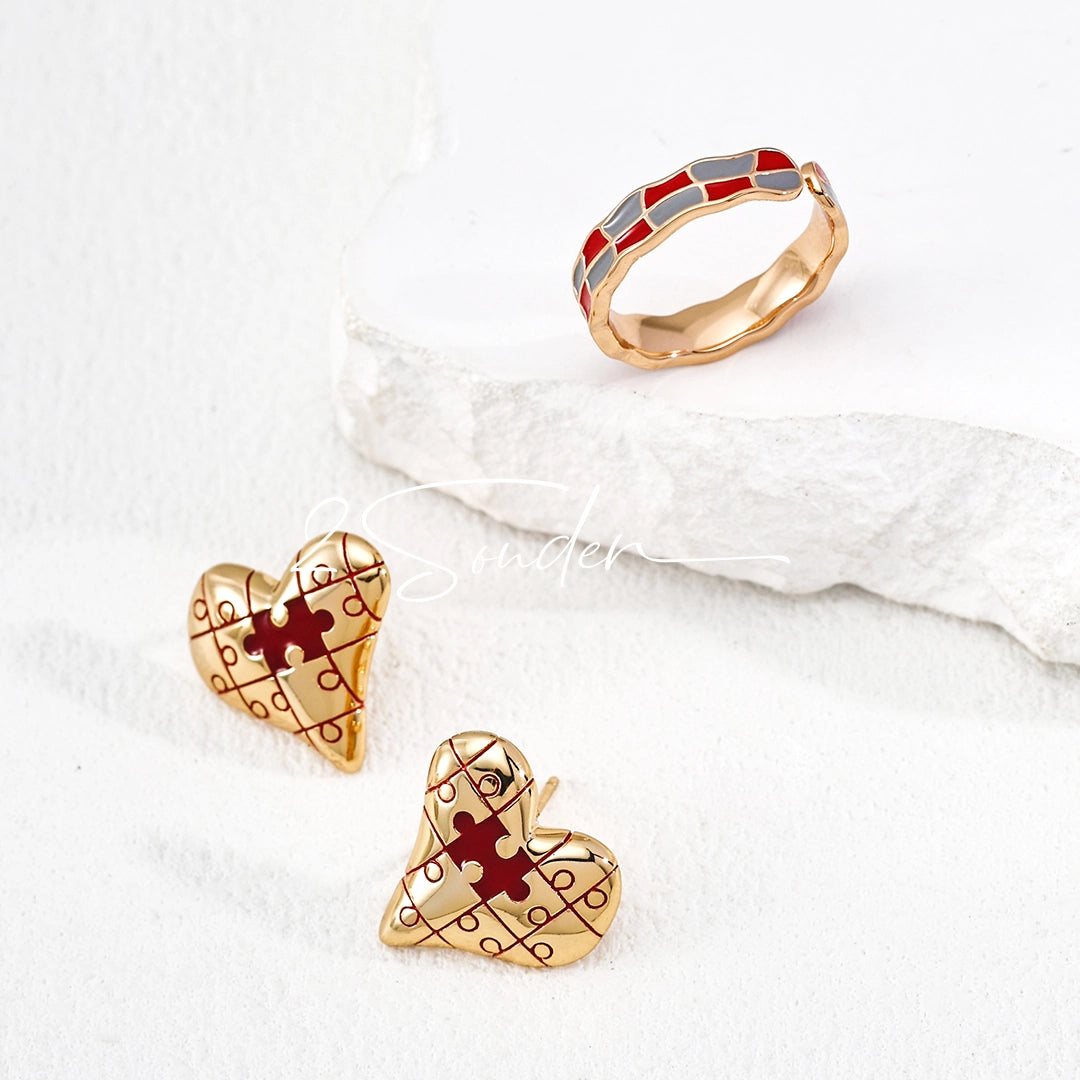 This is a pair of heart earrings with puzzle blocks pattern on the surface. The earrings feature a vibrant enamel center that mimics a beating heart flowing with love. The material of the earrings is sterling silver and enamel, and the color is vintage gold color