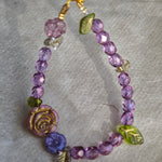 A purple hand-strung bracelet with luminous Czech glass beads & delicate botanical charms.