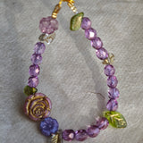 A purple hand-strung bracelet with luminous Czech glass beads & delicate botanical charms.