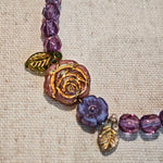 A purple hand-strung bracelet with luminous Czech glass beads & delicate botanical charms.