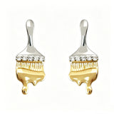 These stud earrings are designed in the shape of a paintbrush, featuring a two-tone finish with a polished silver-toned handle and a gold-toned brush head. The ferrule of the brush is encrusted with sparkling cubic zirconia stones, and the gold-toned bristles are styled to look like dripping, liquid gold paint, creating a vivid, artistic effect. Crafted with a thick 18K real gold plating, they combine a playful, creative design with elegant, eye-catching sparkle.