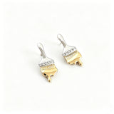 These stud earrings are designed in the shape of a paintbrush, featuring a two-tone finish with a polished silver-toned handle and a gold-toned brush head. The ferrule of the brush is encrusted with sparkling cubic zirconia stones, and the gold-toned bristles are styled to look like dripping, liquid gold paint, creating a vivid, artistic effect. Crafted with a thick 18K real gold plating, they combine a playful, creative design with elegant, eye-catching sparkle.