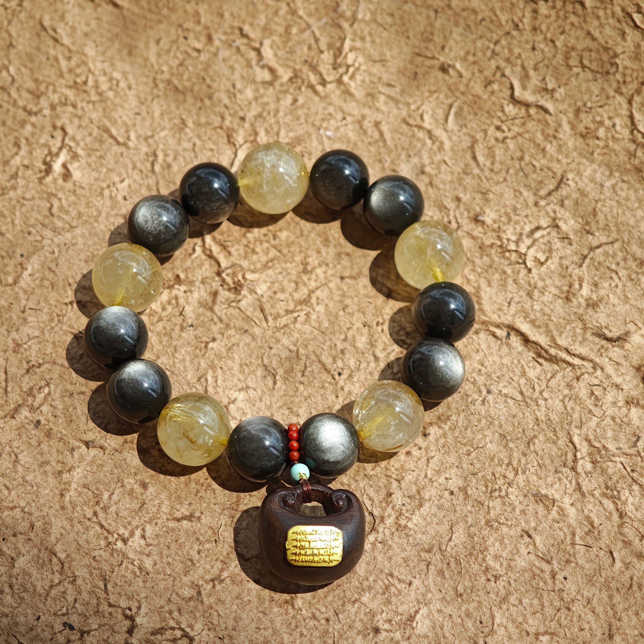 Bold 12 mm silver-sheen obsidian locks arms with 13–13.8 mm golden rutile quartz, crowned by an agarwood bead and Nanhong agate charm—luxury forged in primal power.