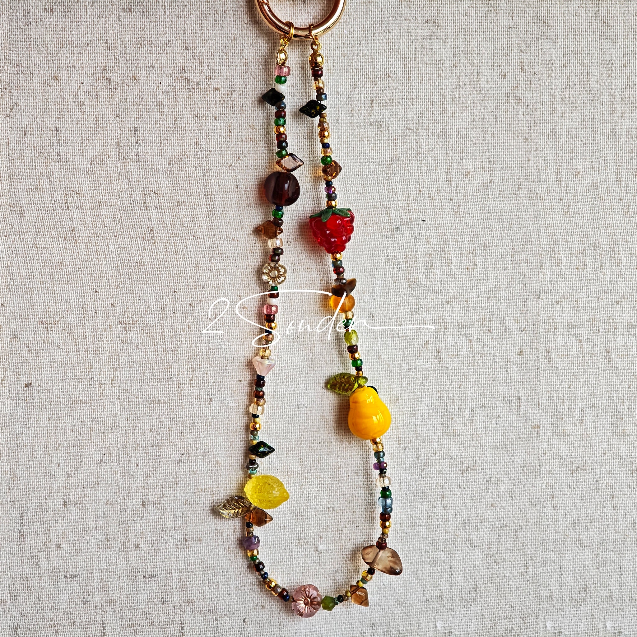This handmade Czech glass bead bag charm is also perfect as a phone strap, keychain accessory, or a car decor. Featuring translucent beads, fruity spacers (pear, lemon, strawberry!), whimsical floral leaves and durable gold-tone hardware, it’s like wearing a garden on your keys.