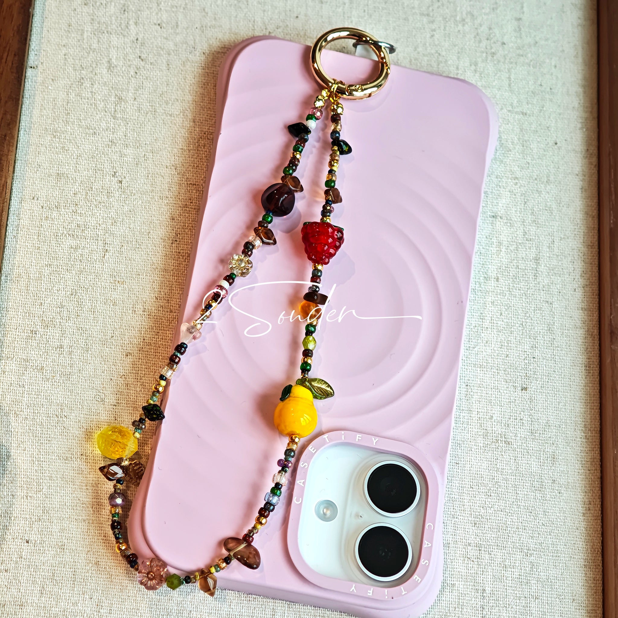 This handmade Czech glass bead bag charm is also perfect as a phone strap, keychain accessory, or a car decor. Featuring translucent beads, fruity spacers (pear, lemon, strawberry!), whimsical floral leaves and durable gold-tone hardware, it’s like wearing a garden on your keys.