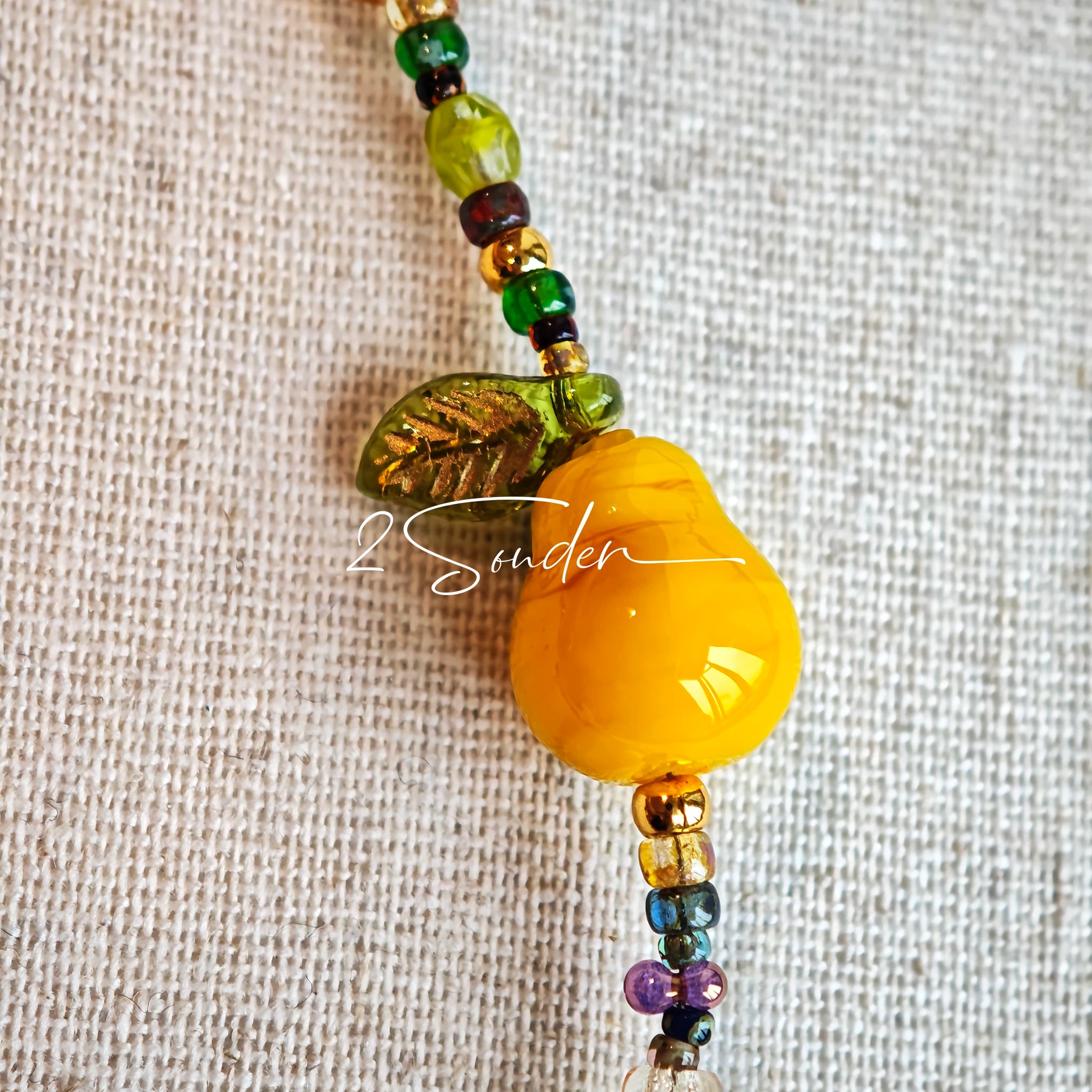 This handmade Czech glass bead bag charm is also perfect as a phone strap, keychain accessory, or a car decor. Featuring translucent beads, fruity spacers (pear, lemon, strawberry!), whimsical floral leaves and durable gold-tone hardware, it’s like wearing a garden on your keys.