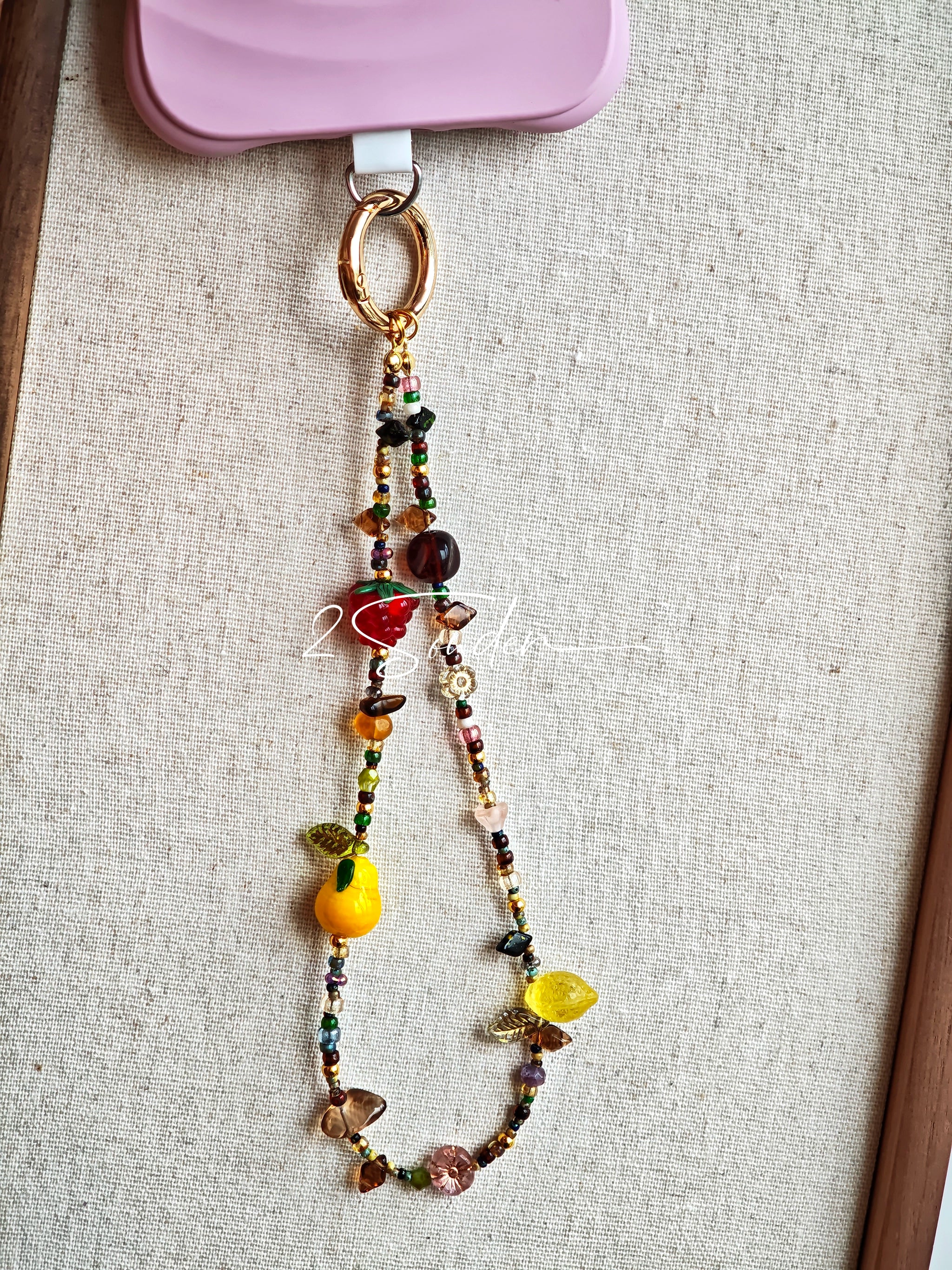 This handmade Czech glass bead bag charm is also perfect as a phone strap, keychain accessory, or a car decor. Featuring translucent beads, fruity spacers (pear, lemon, strawberry!), whimsical floral leaves and durable gold-tone hardware, it’s like wearing a garden on your keys.