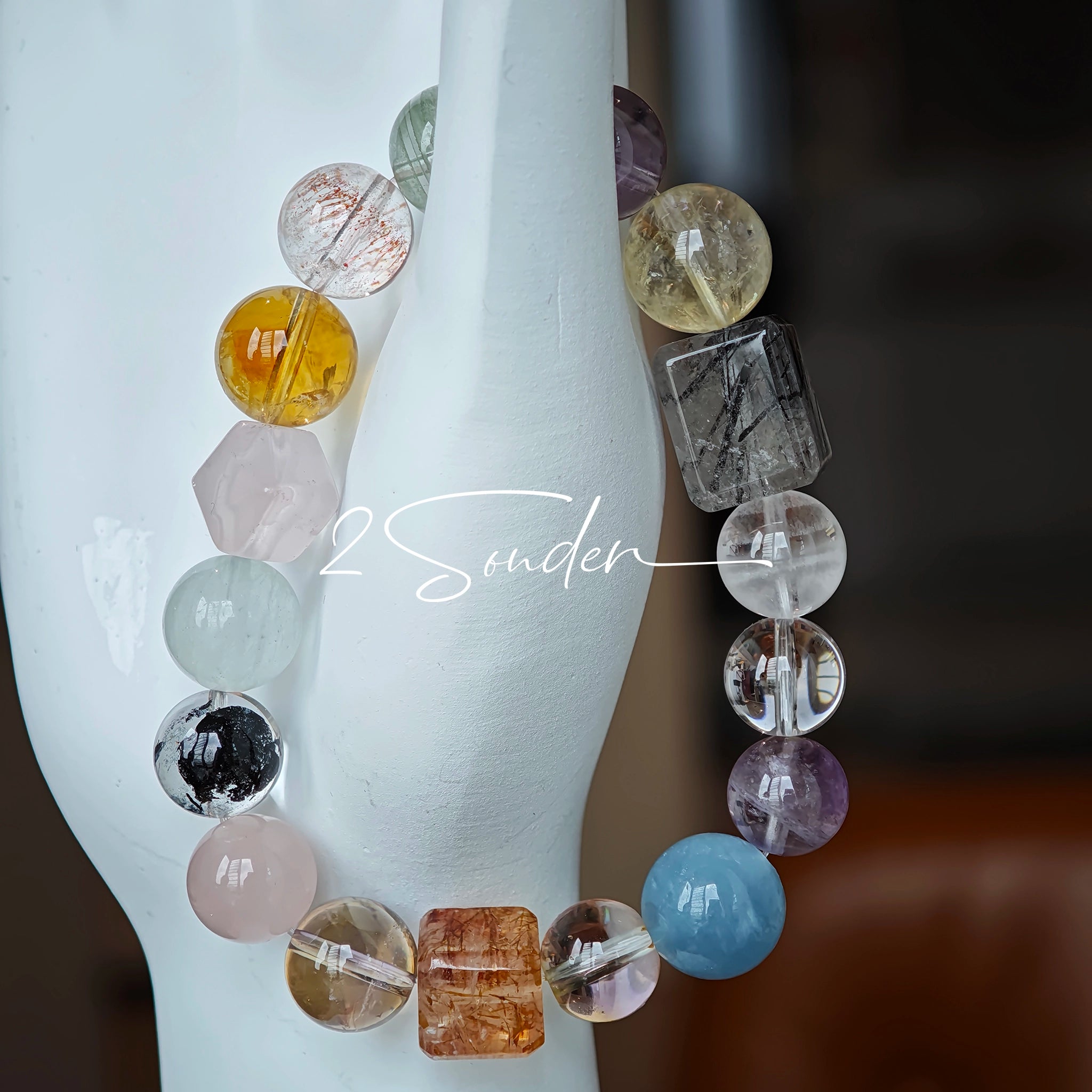 This stunning multi-gem crystal bracelet is a vibrant rainbow of natural stones, featuring smooth round beads in hues of clear, amethyst, sky blue, soft pink, golden, and smoky brown, interspersed with striking square and geometric-cut accents.
Each bead showcases unique inclusions: delicate black rutile in the gray square, fiery red hair-like strands in the brown square, and subtle mineral veining throughout, creating a one-of-a-kind, textured masterpiece.
The eclectic mix of gemstones—from amethyst and ro