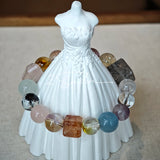This stunning multi-gem crystal bracelet is a vibrant rainbow of natural stones, featuring smooth round beads in hues of clear, amethyst, sky blue, soft pink, golden, and smoky brown, interspersed with striking square and geometric-cut accents.
Each bead showcases unique inclusions: delicate black rutile in the gray square, fiery red hair-like strands in the brown square, and subtle mineral veining throughout, creating a one-of-a-kind, textured masterpiece.
The eclectic mix of gemstones—from amethyst and ro