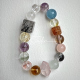 This stunning multi-gem crystal bracelet is a vibrant rainbow of natural stones, featuring smooth round beads in hues of clear, amethyst, sky blue, soft pink, golden, and smoky brown, interspersed with striking square and geometric-cut accents.
Each bead showcases unique inclusions: delicate black rutile in the gray square, fiery red hair-like strands in the brown square, and subtle mineral veining throughout, creating a one-of-a-kind, textured masterpiece.
The eclectic mix of gemstones—from amethyst and ro