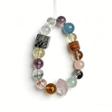 This stunning multi-gem crystal bracelet is a vibrant rainbow of natural stones, featuring smooth round beads in hues of clear, amethyst, sky blue, soft pink, golden, and smoky brown, interspersed with striking square and geometric-cut accents.
Each bead showcases unique inclusions: delicate black rutile in the gray square, fiery red hair-like strands in the brown square, and subtle mineral veining throughout, creating a one-of-a-kind, textured masterpiece.
The eclectic mix of gemstones—from amethyst and ro