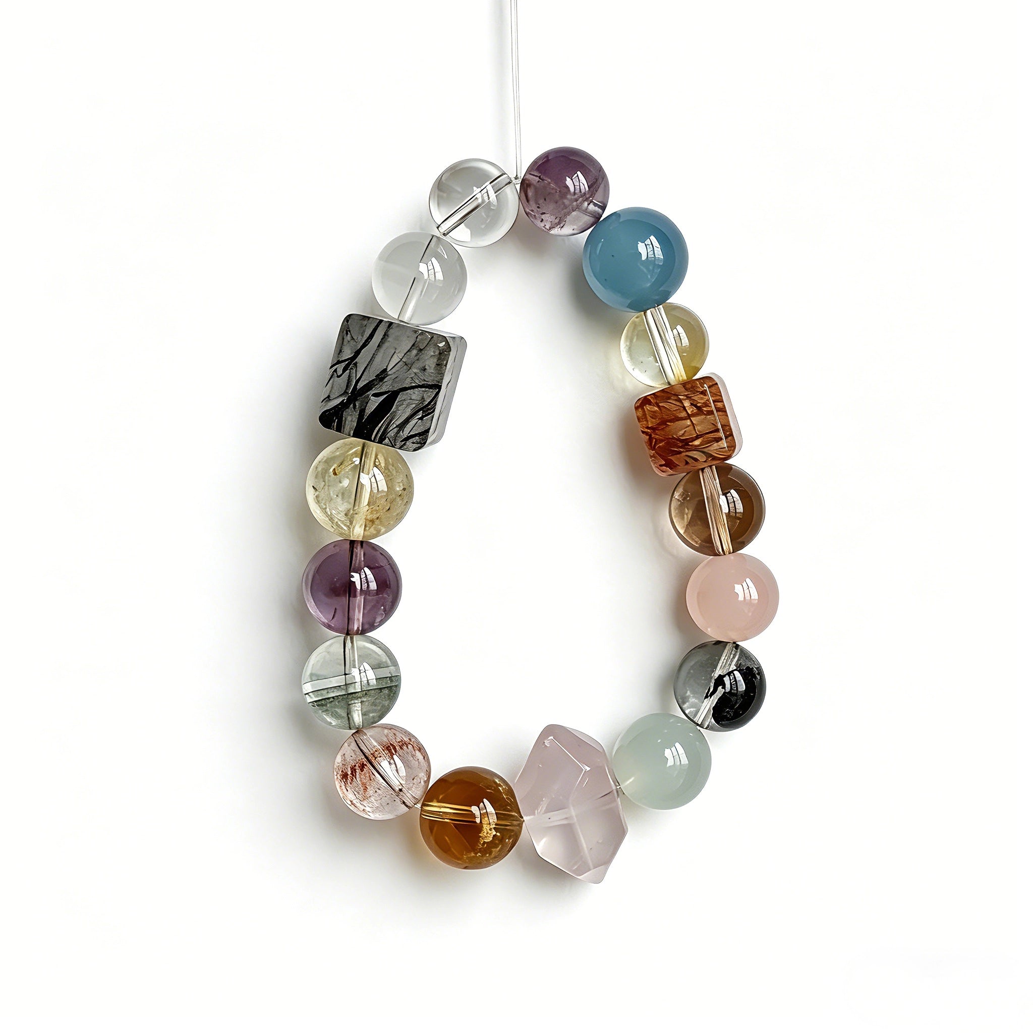 This stunning multi-gem crystal bracelet is a vibrant rainbow of natural stones, featuring smooth round beads in hues of clear, amethyst, sky blue, soft pink, golden, and smoky brown, interspersed with striking square and geometric-cut accents.
Each bead showcases unique inclusions: delicate black rutile in the gray square, fiery red hair-like strands in the brown square, and subtle mineral veining throughout, creating a one-of-a-kind, textured masterpiece.
The eclectic mix of gemstones—from amethyst and ro