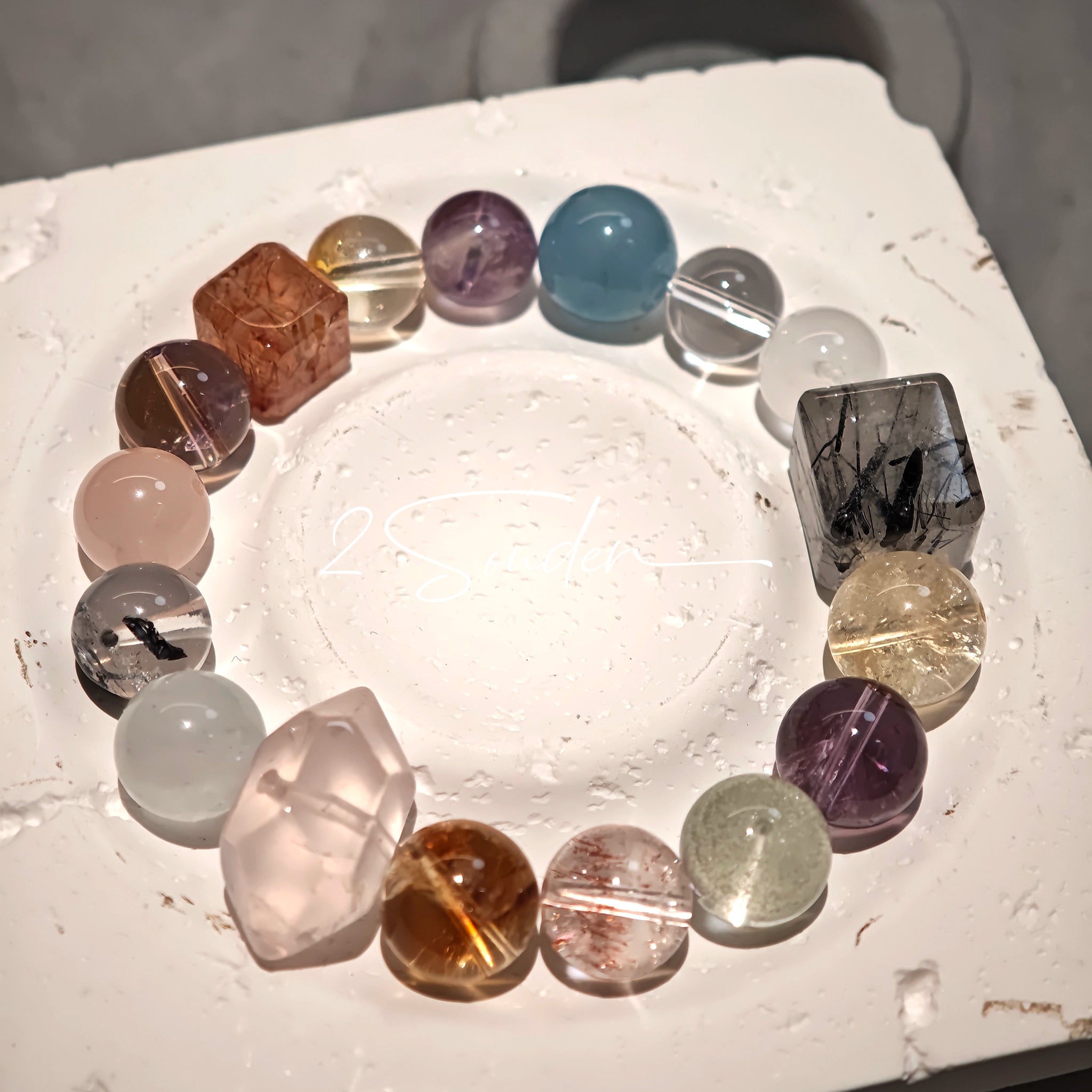 This stunning multi-gem crystal bracelet is a vibrant rainbow of natural stones, featuring smooth round beads in hues of clear, amethyst, sky blue, soft pink, golden, and smoky brown, interspersed with striking square and geometric-cut accents.
Each bead showcases unique inclusions: delicate black rutile in the gray square, fiery red hair-like strands in the brown square, and subtle mineral veining throughout, creating a one-of-a-kind, textured masterpiece.
The eclectic mix of gemstones—from amethyst and ro