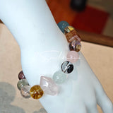 This stunning multi-gem crystal bracelet is a vibrant rainbow of natural stones, featuring smooth round beads in hues of clear, amethyst, sky blue, soft pink, golden, and smoky brown, interspersed with striking square and geometric-cut accents.
Each bead showcases unique inclusions: delicate black rutile in the gray square, fiery red hair-like strands in the brown square, and subtle mineral veining throughout, creating a one-of-a-kind, textured masterpiece.
The eclectic mix of gemstones—from amethyst and ro