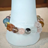 This stunning multi-gem crystal bracelet is a vibrant rainbow of natural stones, featuring smooth round beads in hues of clear, amethyst, sky blue, soft pink, golden, and smoky brown, interspersed with striking square and geometric-cut accents.
Each bead showcases unique inclusions: delicate black rutile in the gray square, fiery red hair-like strands in the brown square, and subtle mineral veining throughout, creating a one-of-a-kind, textured masterpiece.
The eclectic mix of gemstones—from amethyst and ro