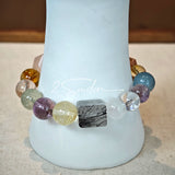 This stunning multi-gem crystal bracelet is a vibrant rainbow of natural stones, featuring smooth round beads in hues of clear, amethyst, sky blue, soft pink, golden, and smoky brown, interspersed with striking square and geometric-cut accents.
Each bead showcases unique inclusions: delicate black rutile in the gray square, fiery red hair-like strands in the brown square, and subtle mineral veining throughout, creating a one-of-a-kind, textured masterpiece.
The eclectic mix of gemstones—from amethyst and ro