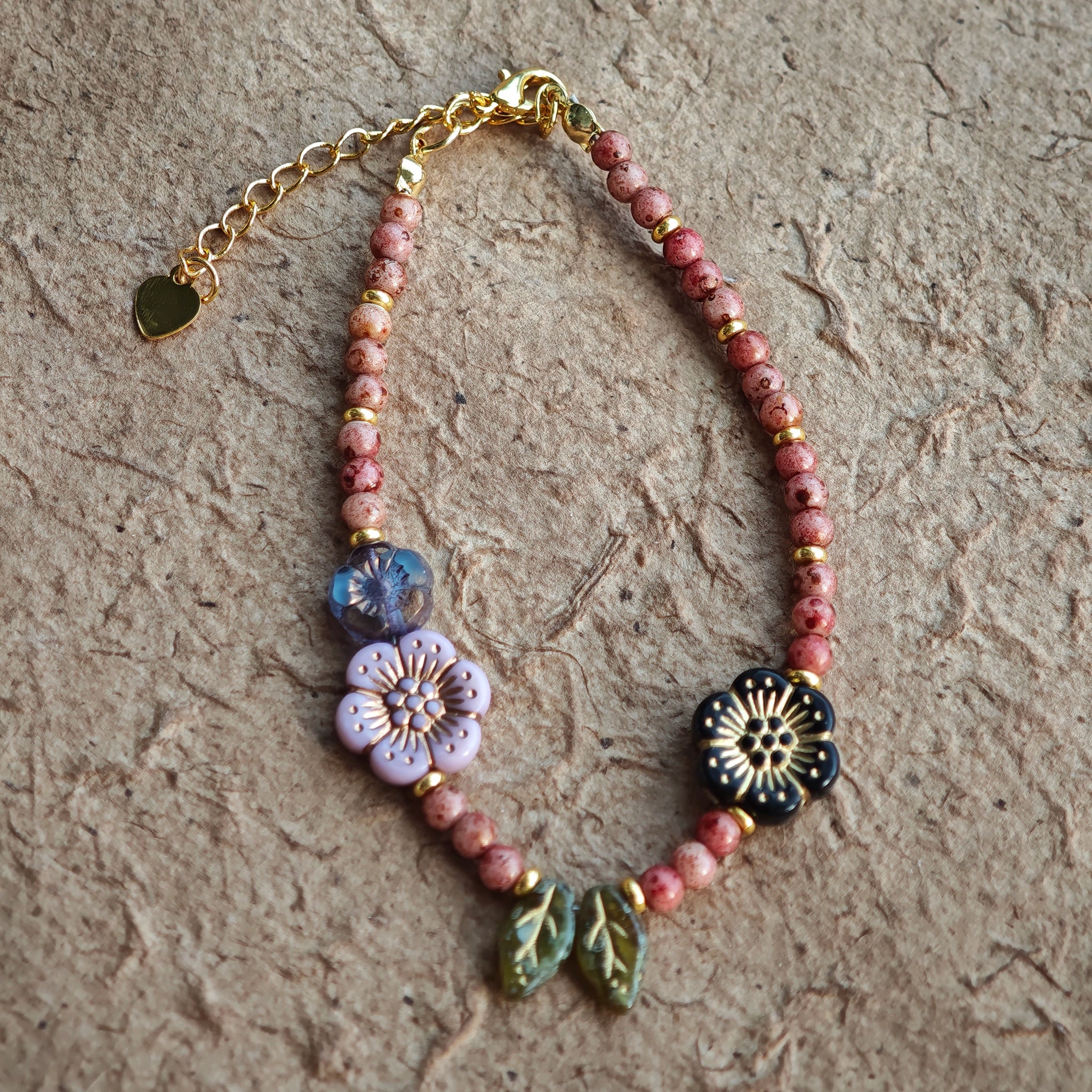 Vibrant pink Czech glass beads are highlighted by blue, purple, and black flower charms and green leaf accents, creating a stunningly attractive design.