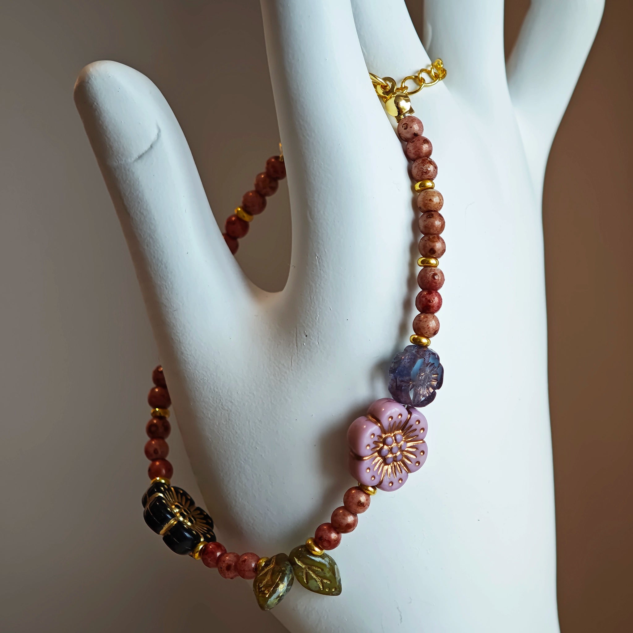 Vibrant pink Czech glass beads are highlighted by blue, purple, and black flower charms and green leaf accents, creating a stunningly attractive design.