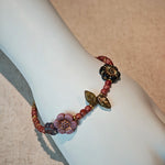 Vibrant pink Czech glass beads are highlighted by blue, purple, and black flower charms and green leaf accents, creating a stunningly attractive design.