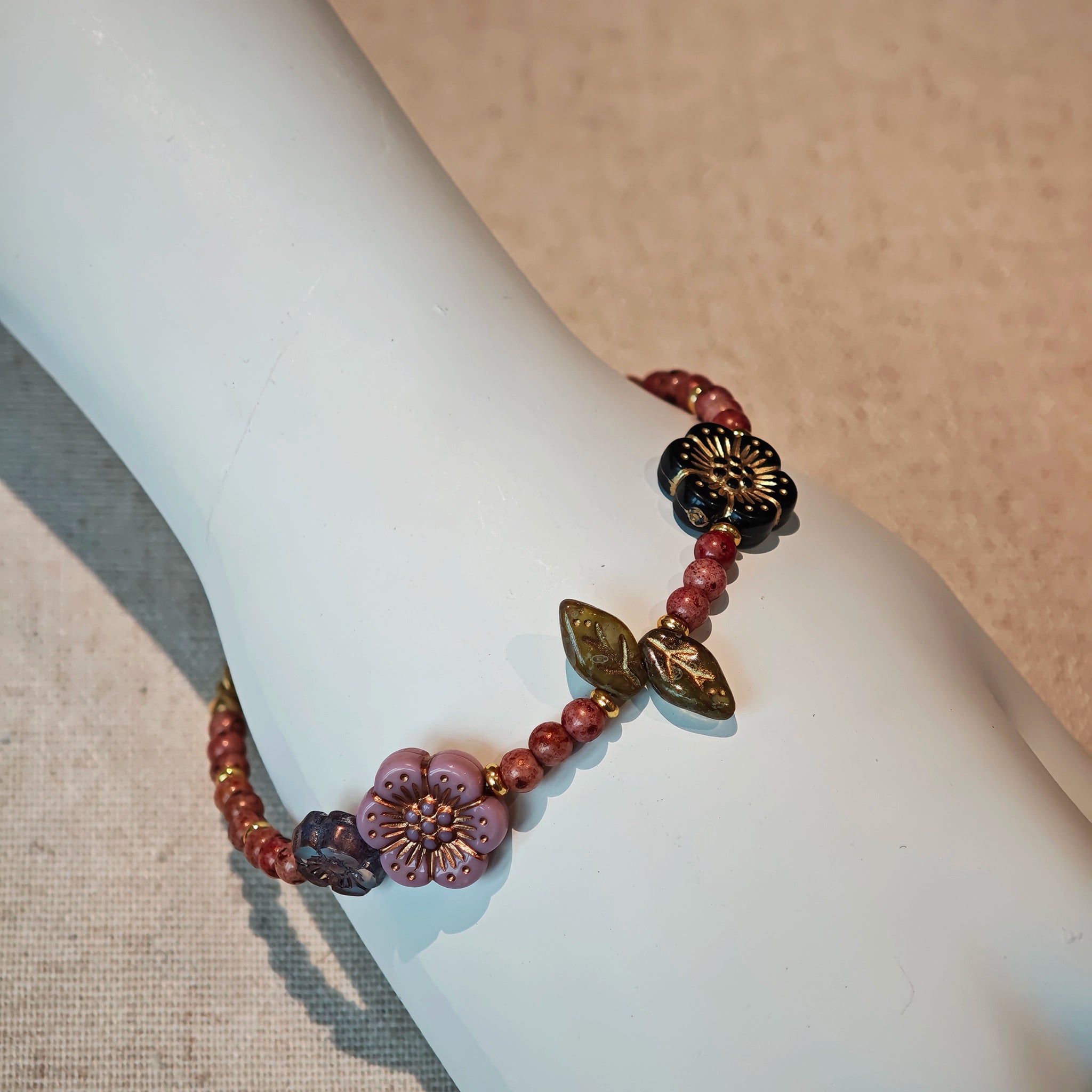 Vibrant pink Czech glass beads are highlighted by blue, purple, and black flower charms and green leaf accents, creating a stunningly attractive design.