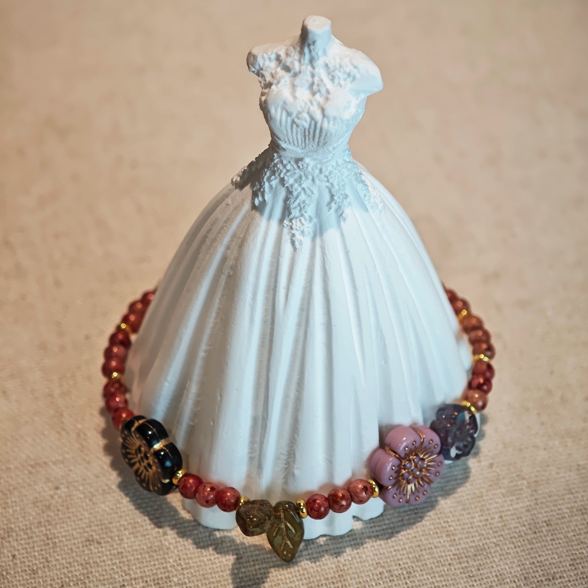 Vibrant pink Czech glass beads are highlighted by blue, purple, and black flower charms and green leaf accents, creating a stunningly attractive design.