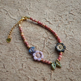Vibrant pink Czech glass beads are highlighted by blue, purple, and black flower charms and green leaf accents, creating a stunningly attractive design.
