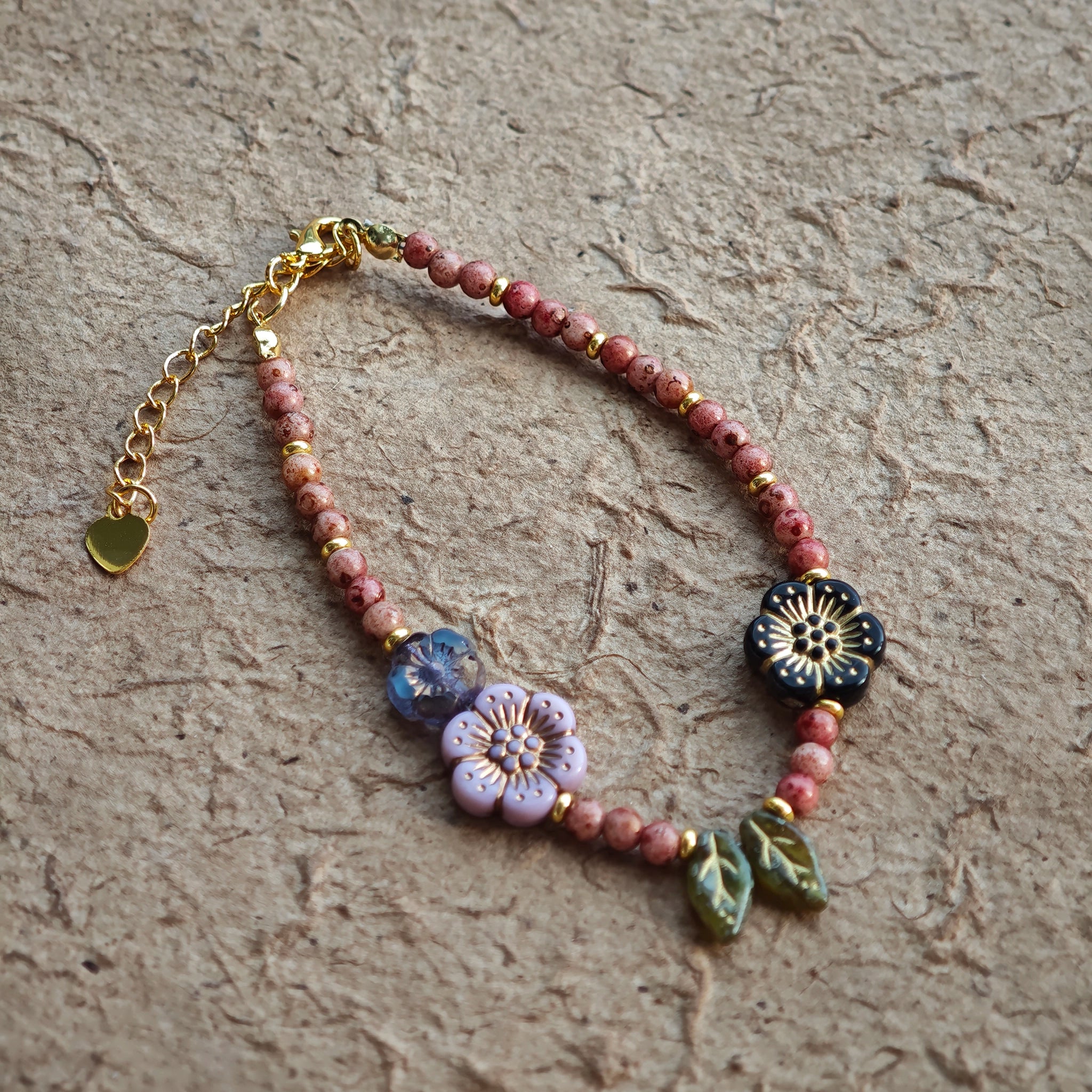 Vibrant pink Czech glass beads are highlighted by blue, purple, and black flower charms and green leaf accents, creating a stunningly attractive design.