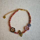 Vibrant pink Czech glass beads are highlighted by blue, purple, and black flower charms and green leaf accents, creating a stunningly attractive design.