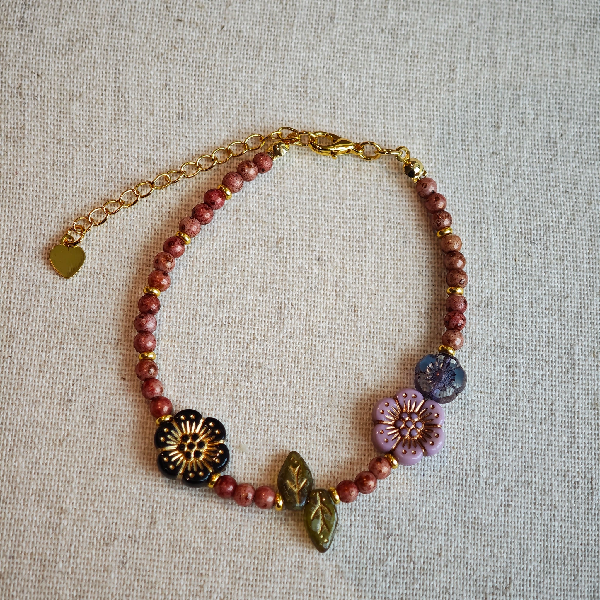 Vibrant pink Czech glass beads are highlighted by blue, purple, and black flower charms and green leaf accents, creating a stunningly attractive design.